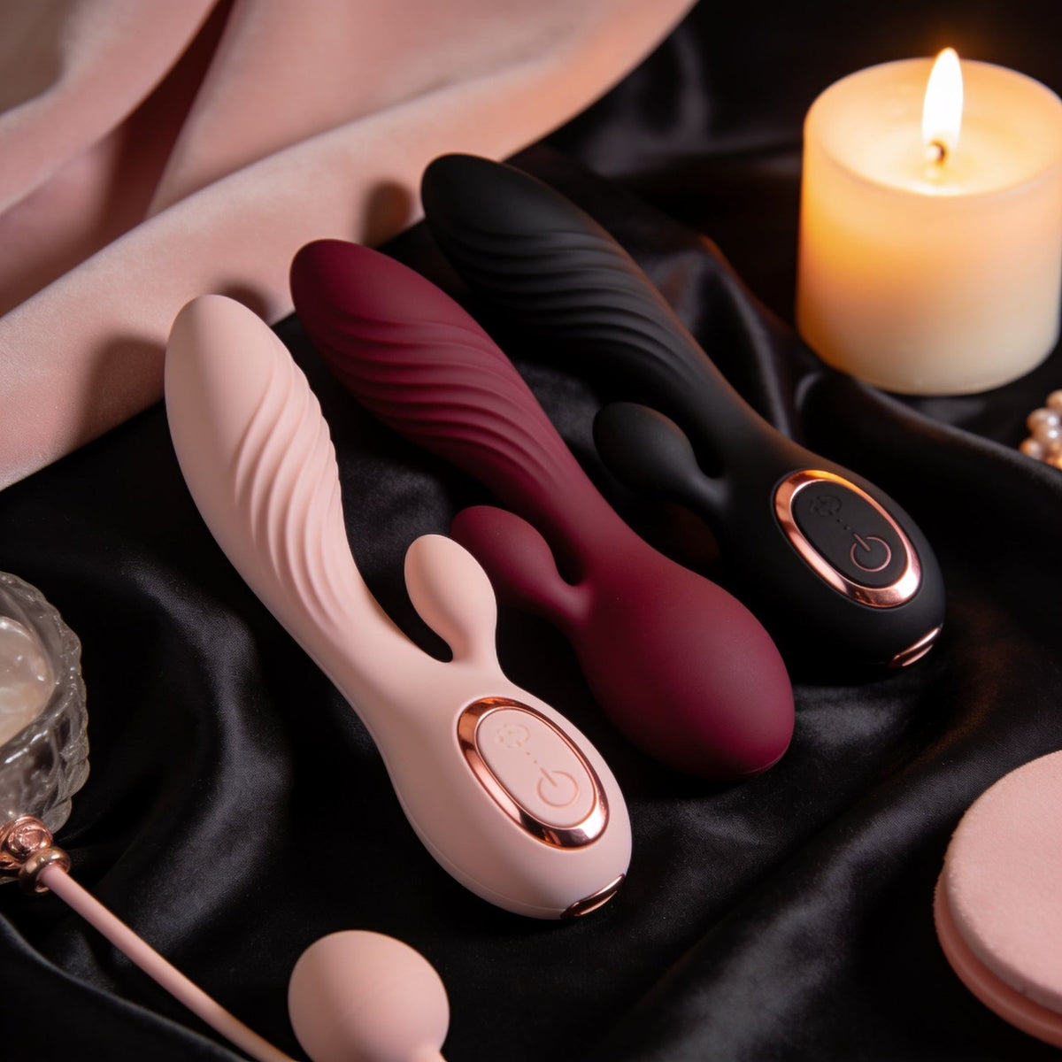 Premium vibrators in blush pink, deep burgundy and matte black with rose-gold accents, elegantly styled on black satin beside soft candlelight for a luxurious intimate wellness aesthetic.